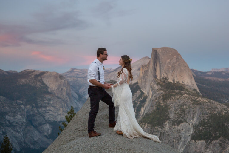 A bride and groom stand facing each other and holding hands at Glacier Point on their Yosemite elopement day.