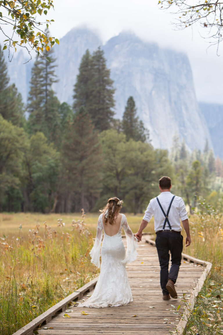 A bride and groom walk down a wooden boardwalk in Yosemite